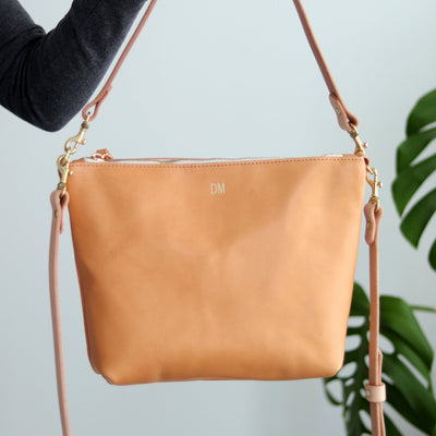 Beige colored natural vegetable tanned leather handbag with gold foil monogram.  Minimalist and simple women's crossbody bag with top zipper, shoulder strap and crossbody strap.