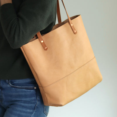 Beige vacchetta leather tote bag handcrafted from full-grain vegetable-tanned leather with hand-burnished straps and copper rivets.