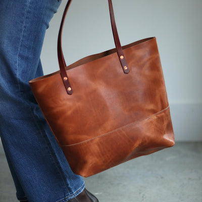 Full-grain vegetable-tanned distressed brown leather tote showing natural markings and hand-burnished straps.