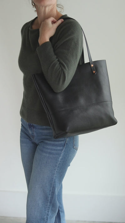 All-black Italian pebbled leather tote with matching black bridle straps and copper rivets.