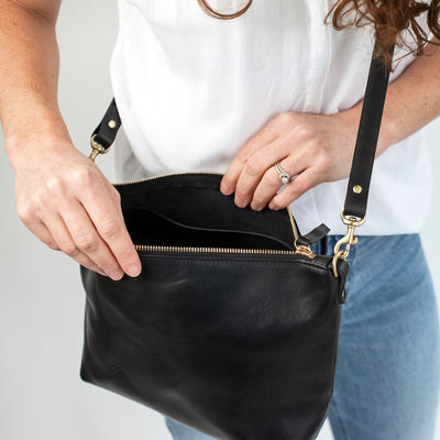 Juliette Rose Designs black leather handbag.  Woman in casual outfit of jeans and white shirt looking inside her black leather handbag with top zipper.