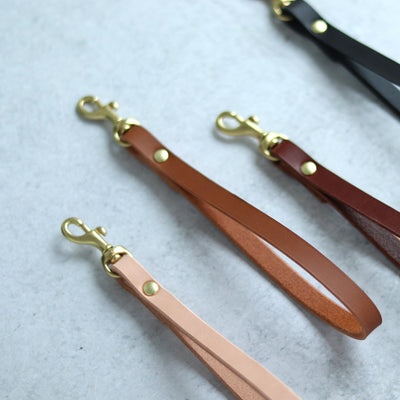 Leather wrist straps handmade with vegetable tanned leather and brass and gold hardware. Add a slim leather wrist strap to your clutch bag, by Juliette Rose Designs. 4 colors are available in black, cognac brown, tan, and natural beige.